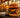 Saftiger Double-Smash-Burger mit geschmolzenem Cheddar, karamellisierten Zwiebeln und Brioche-Bun, daneben Pommes im Drahtkorb und Aioli, im Hintergrund Beachbar mit Palmen und Sonnenuntergang an der Playa de Palma – Beste Burger auf Mallorca